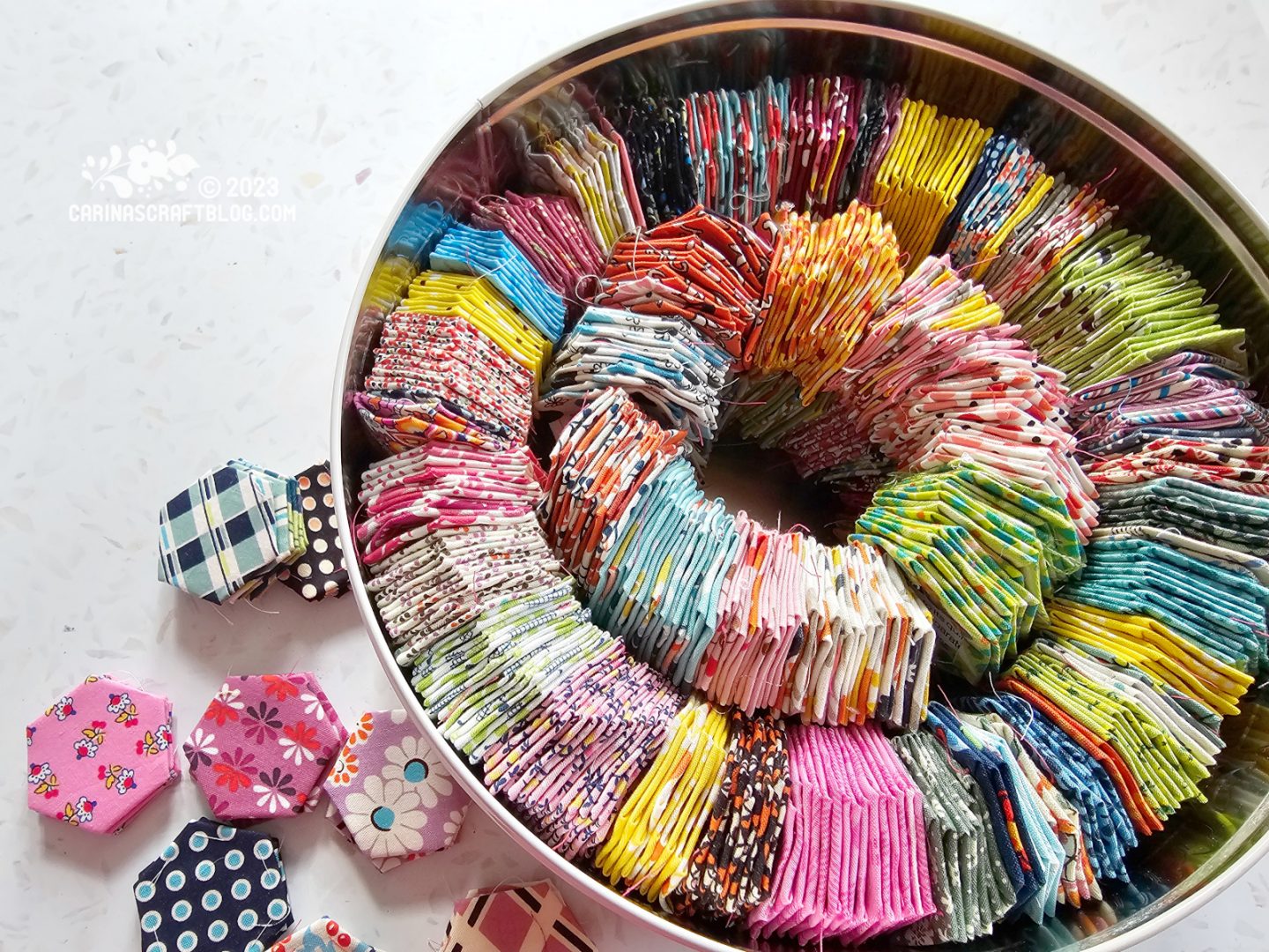 Overhead view of a large biscuit tin filled with fabric hexagons in many different prints and colours.