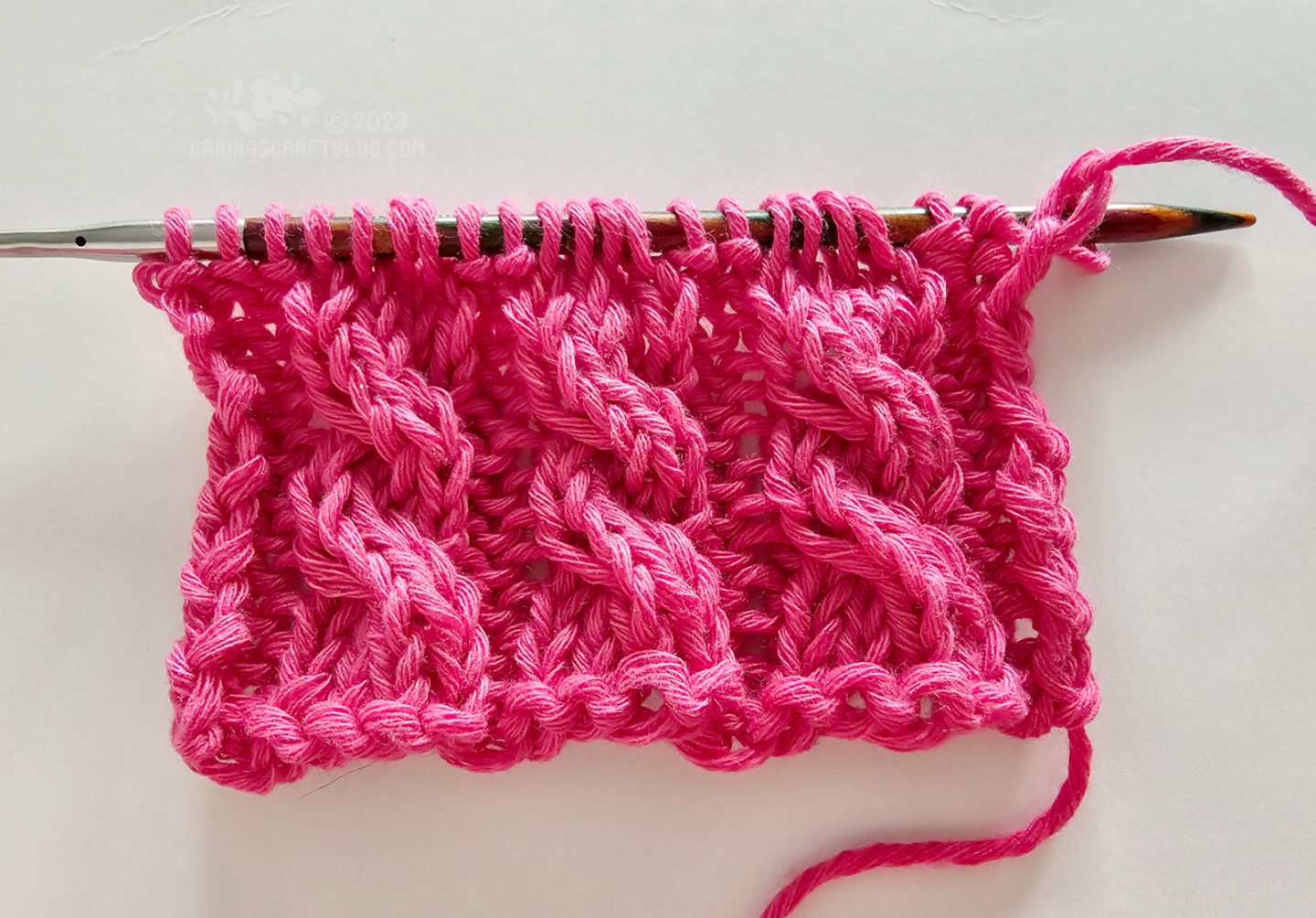 Overhead view of a short piece of knitting with a cabled pattern  using hot pink year.