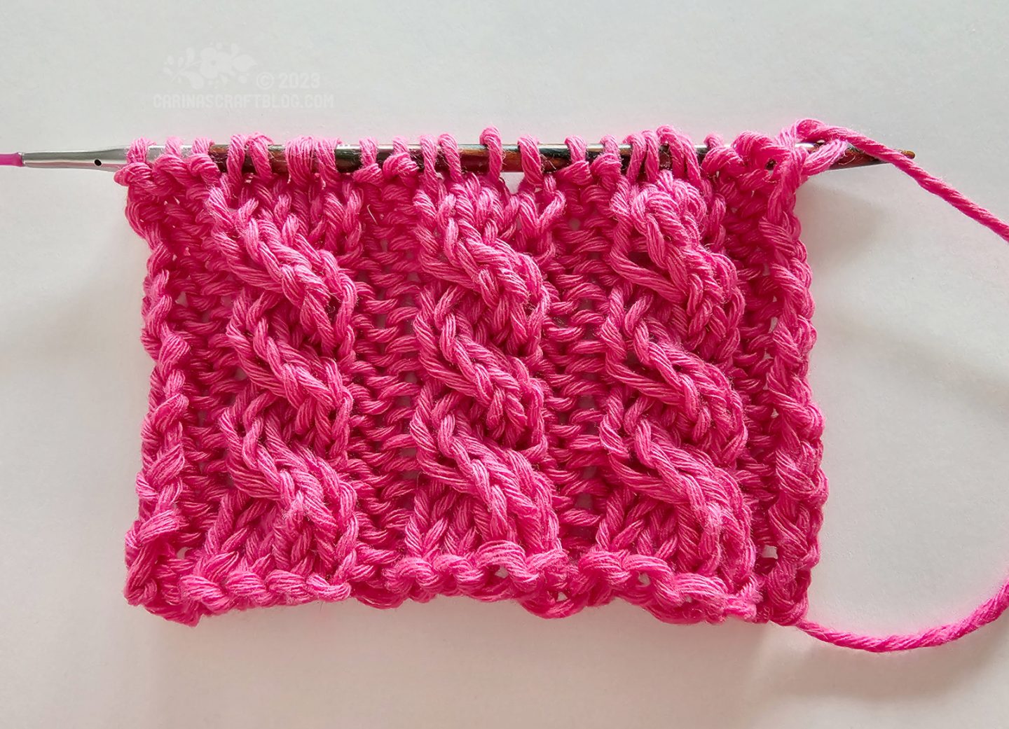 Overhead view of a short piece of knitting with a cabled pattern using hot pink year.