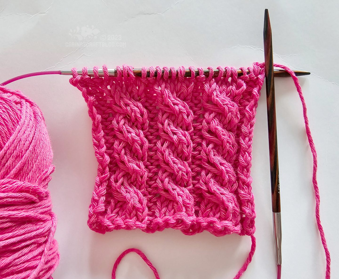 Overhead view of a short piece of knitting with a cabled pattern using hot pink year.