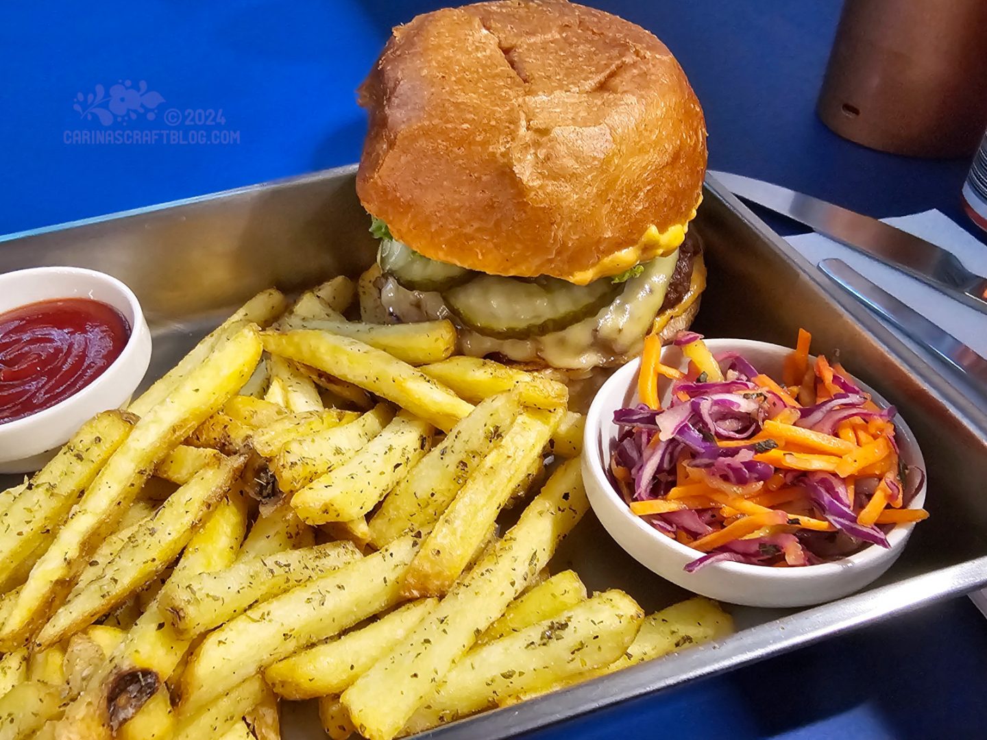 Close view of a metal tray with fries, a burger and a small bowl of shredded carrots and red cabbage.