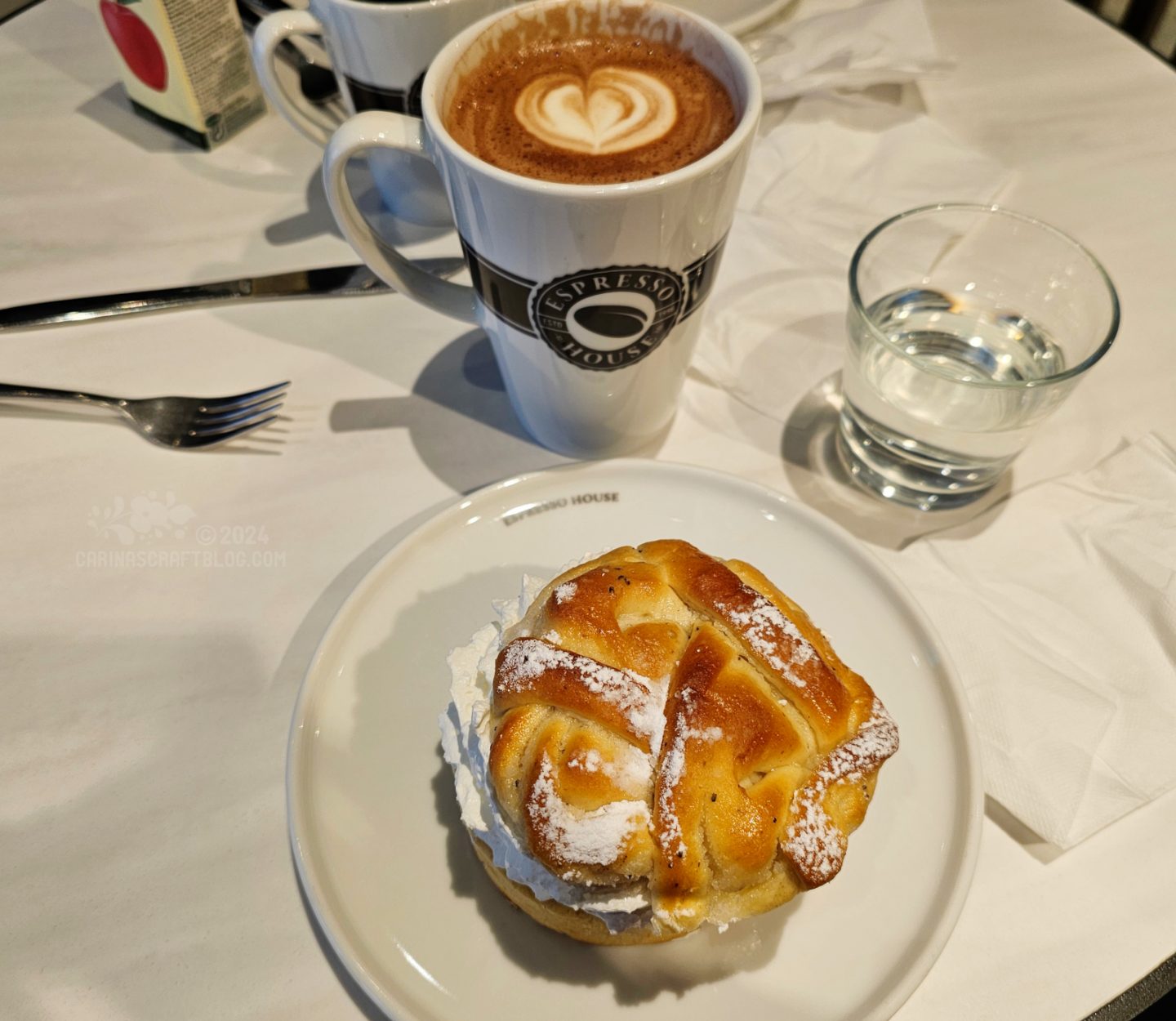 Picture of a plate with a bun with whipped cream and a mug of hot chocolate.