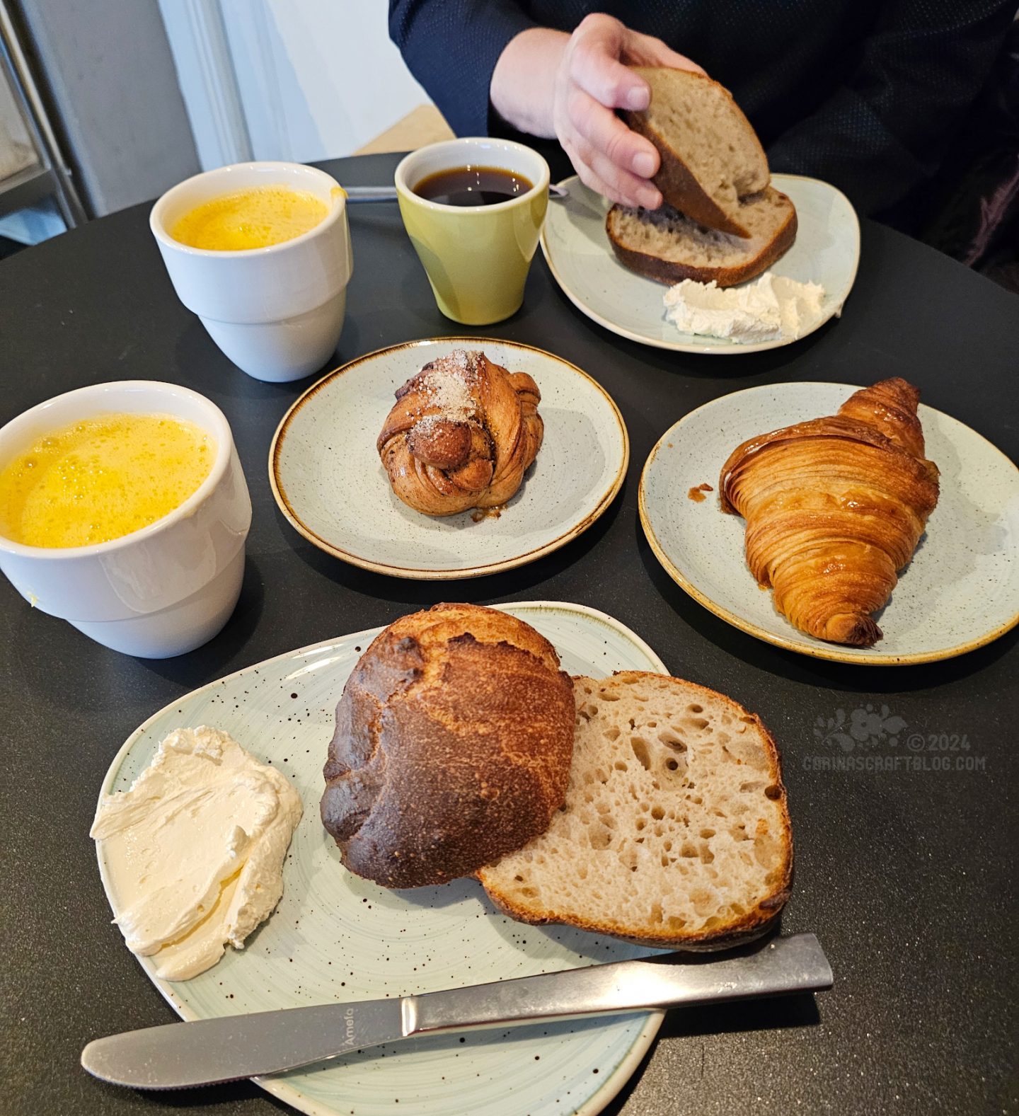 Overhead view of a table with breakfast foods: rolls, croissants and mugs of coffee and orange juice.